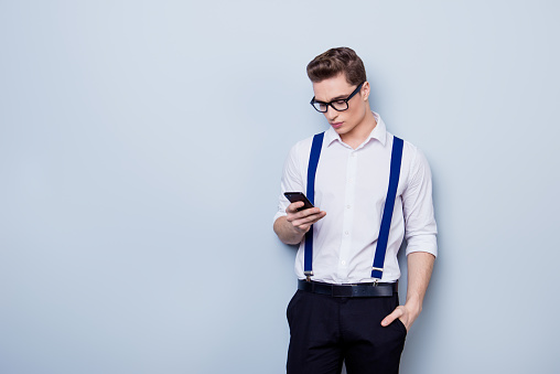 Young attractive guy in glasses and formal wear is looking at his phone. He is serious and reading message