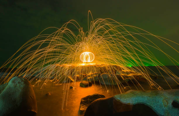 огненный шар у скал у моря - water fire circle ball стоковые фото и изображения