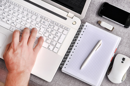 Human hands typing on a white laptop keyboard with isolated screen.Working desk table concept.High above view of office workplace with phone and mouse with notebook, pen and usb flash on grey desk.