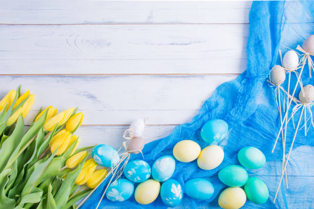istock Easter eggs on white wooden background. Colorful eatser eggs ian yellow tulips. Eatser card. 940532070