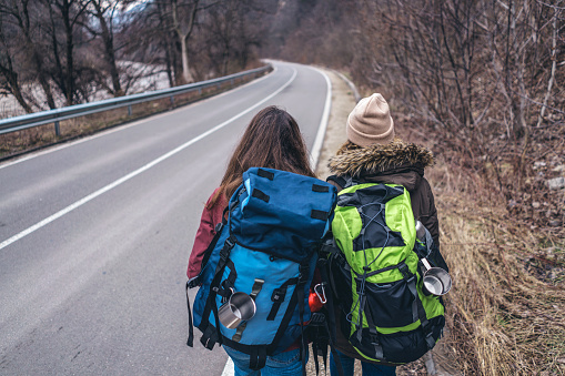 Rear view image of female couple with heavy hiking rucksacks walking on the country road