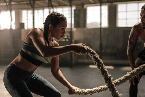 Powerful muscular woman exercising with battle ropes at the gym with personal trainer. Battle rope workout at gym with instructor.
