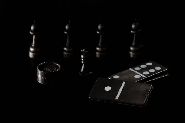 Photo of dice dominoes checkers and chess pieces on a dark background