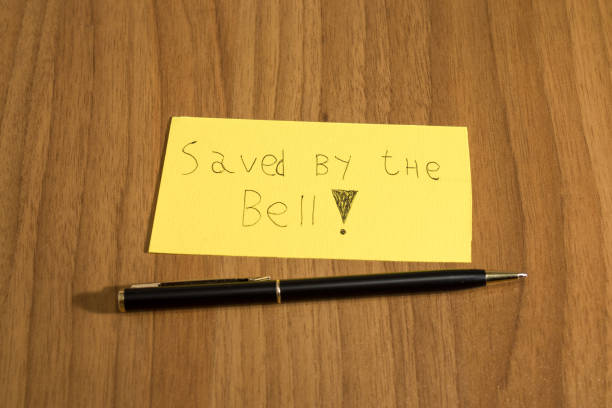 istock Sanved by the bell, handwrite on a yellow paper with a pen on a table composition 940556040