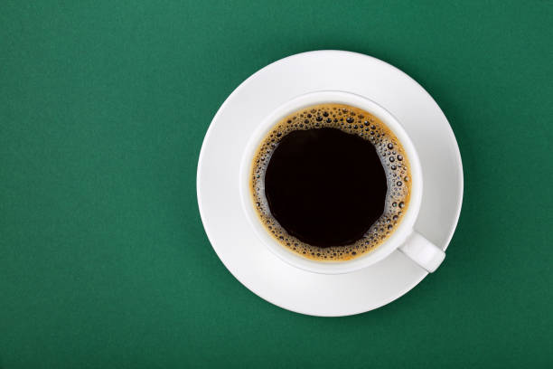 istock White cup of black coffee on saucer over green 940559824