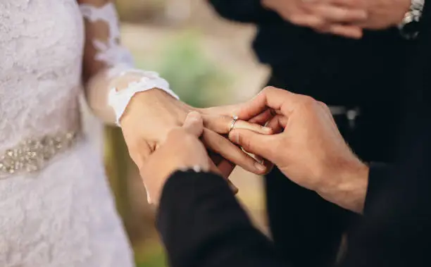 Closeup of groom placing a wedding ring on the brides hand.  Couple exchanging wedding rings during a wedding ceremony outdoors.