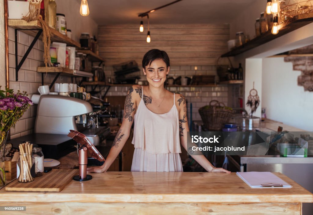 Woman entrepreneur standing at the billing counter of her cafe Woman standing at the billing counter of her cafe posing. Smiling restaurant owner standing beside the billing machine. Entrepreneur Stock Photo