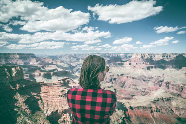 A dramatic overlook over the grand canyon in Arizona USA. A young woman looks over the edge in amazement as she explores the landscape on a solo journey.