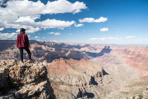 A dramatic overlook over the grand canyon in Arizona USA. A young woman looks over the edge in amazement as she explores the landscape on a solo journey.