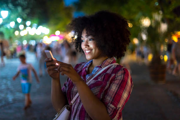 istock Smiling woman using smart phone on street at night 940586358