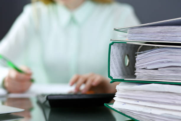 istock Bookkeeper or financial inspector  making report, calculating or checking balance. Binders with papers closeup. Audit and tax service concept. Green colored image backgroun 940590790