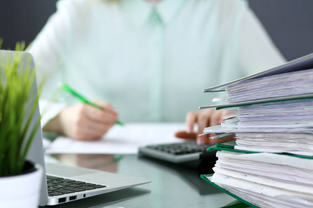 istock Bookkeeper or financial inspector  making report, calculating or checking balance. Binders with papers closeup. Audit and tax service concept. Green colored image backgroun 940590824