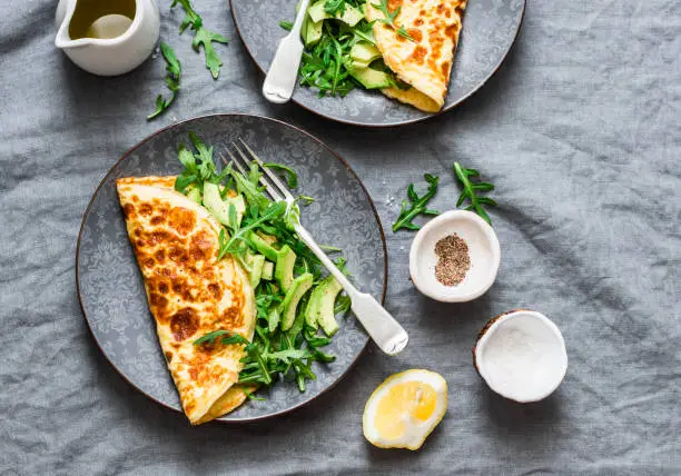 Omelette with cream cheese, arugula and avocado salad on a grey background, top view.  Healthy breakfast or diet lunch