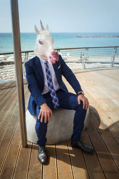 istock Young funny man in elegant suit sits on the city waterfront 940598566