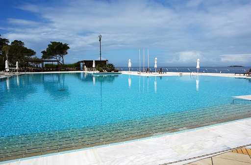 Vouliagmeni, Greece - March 28, 2015: View of the large pool and the blue sea in modern luxury hotel on the Aegean coast.