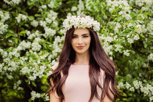 young smiling woman wearing flowers wreath. cute girl with makeup, flowers and long smooth hair on floral background outdoors - beauty queen imagens e fotografias de stock