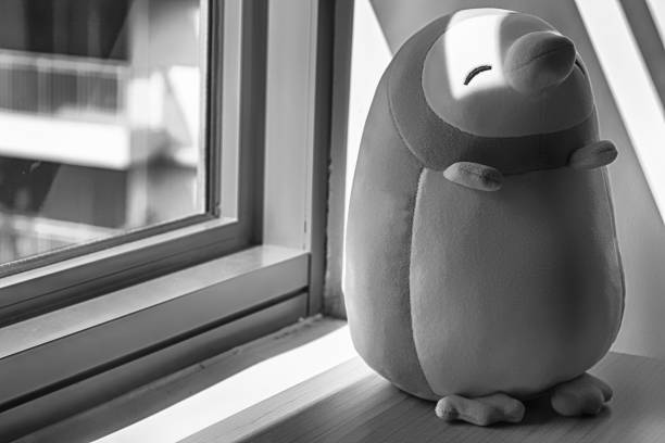 istock Monochrome Penguin toy sitting by the window in shadows 940611380