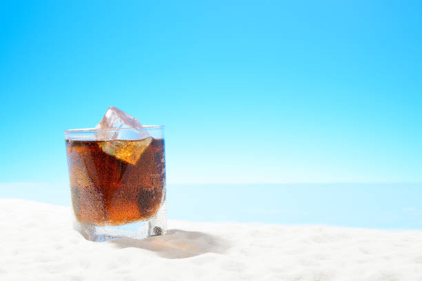 Refreshing Cola with ice in glass on the sandy coast