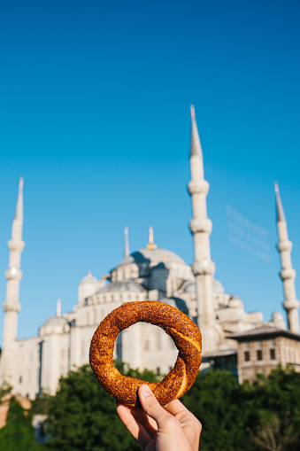 A woman is holding a traditional Turkish bagel named Simit in the background of the Blue Mosque in Istanbul, Turkey. Traditions, tourism,