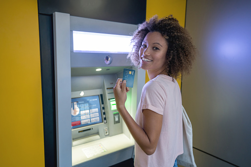 Portrait of a happy woman making a cash withdrawal on an ATM and looking at the camera smiling