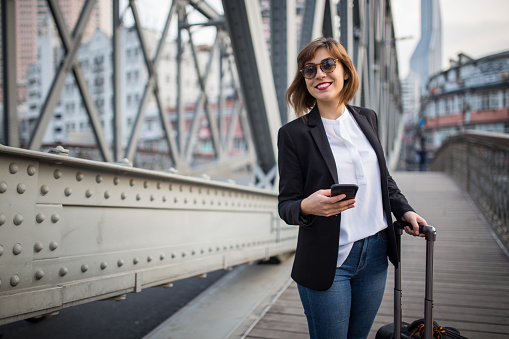Beautiful woman standing on the bridge and holding phone and suitcase