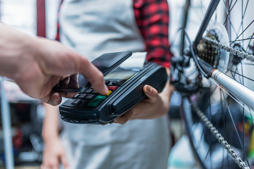 Close up of Female Shop owner accepting payment using credit card. Photo of man inserting credit card in payment machine . Customer and dealer in bicycle shop - purchase and repair of bicycles - customer service.