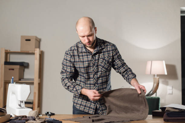 istock The tailor lays out the wool fabric on the cutting table. Young man working as a tailor and using a sewing machine in workshop. 940700328