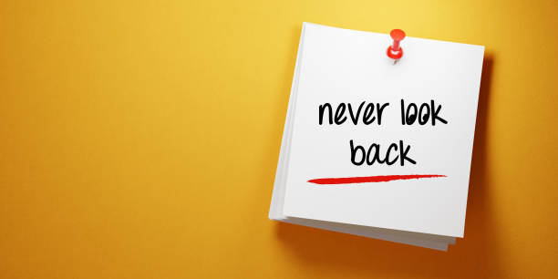 istock White Sticky Note with Never Look Back Message And Red Push Pin On Yellow Background 940700858