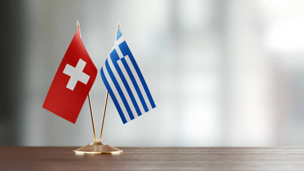 istock Swiss And Greek Flag Pair On A Desk Over Defocused Background 940705352
