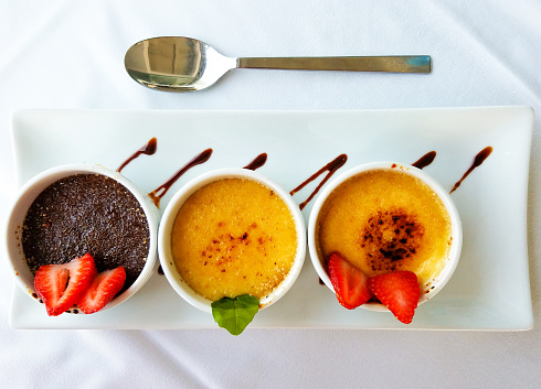 Three cups with creme brulee, strawberries, and cocoa, served on a white rectangle plate.