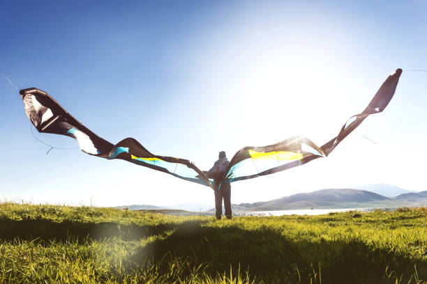 Man or woman stands with kite against blue sky and sun light
