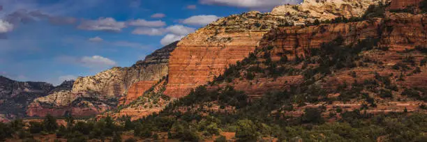 Colorful view of red rock formations cascading into the distance from Vultee Arch hiking trail on a sunny day with blue sky and clouds, Sedona, Arizona