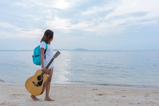 Asian young backpacker holding guitar , walking on the beach