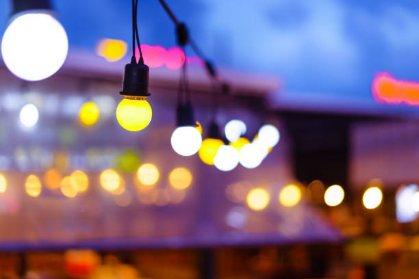 装飾的な屋外の文字列のライトはぼかしの人で夜間電気ポスト庭の上にぶら下がって。クリスマス、お祭り、休日や結婚式の概念。 - 夜市 ストックフォトと画像
