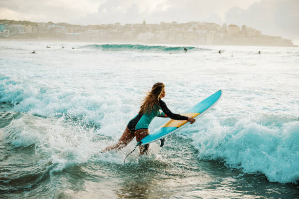 donna surfista salta sulla sua tavola da surf nell'onda - surfing new south wales beach australia foto e immagini stock