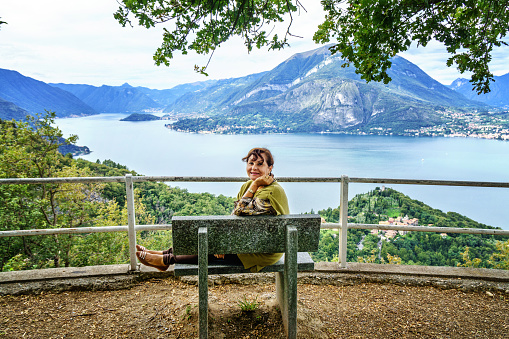 Attractive senior hispanic woman sitting on bench above Lake Como