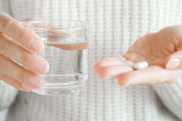 mains de femme tenant un verre d’eau et blanc pilule. réception de vitamines. concept de médecine, de pharmacie et de soins de santé. - painkiller photos et images de collection