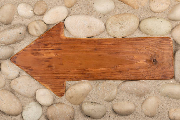 Classical wooden arrow and white stones on the sand. Space for the designer