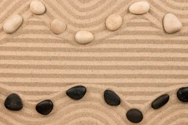 Photo of Two rows of blackand white stones lying on the sand, with space for text.