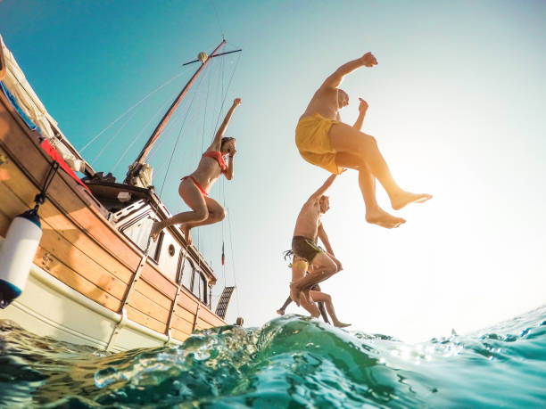 happy vrienden duiken vanaf zeilboot in de zee - jongeren springen binnen oceaan in zomer excursie dag - vakantie, jeugd en leuk concept - main focus op linker man - fisheye-lens vertekening - recreatieboot stockfoto's en -beelden