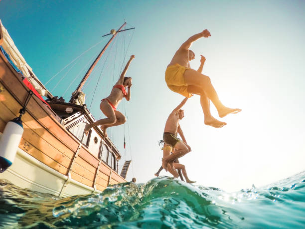 happy friends diving from sailing boat into the sea - young people jumping inside ocean in summer excursion day - vacation, youth and fun concept - main focus on left man - fisheye lens distortion - sailboat sunset sailing nautical vessel imagens e fotografias de stock