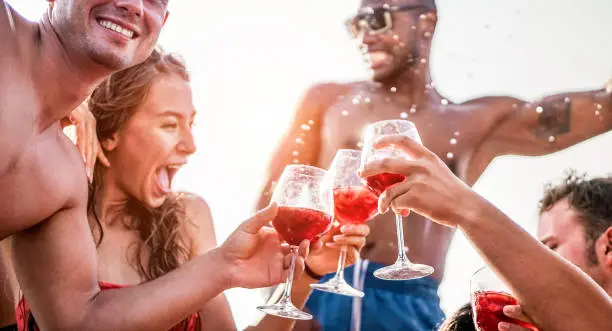Happy friends drinking sangria wine at exclusive boat party - Young people having fun in summer vacation - Focus on left man hand glass - Travel, friendship, holidays and youth lifestyle concept