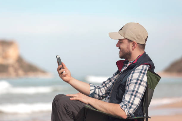 istock Man Sitting at the Beach and Looking his Phone 940949696