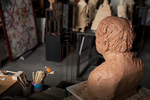 A sculptor's workshop in Provence. A clay bust surveys his place of creation. The various sticks and implements used to create detail on the bust are in a jar and clay figuerines and paintings are in the background.