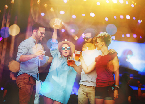 Active people dancing and raising hands while partying in nightclub. Young men and women moving to electronic music beats and relaxing on crowded dancefloor at discotheque