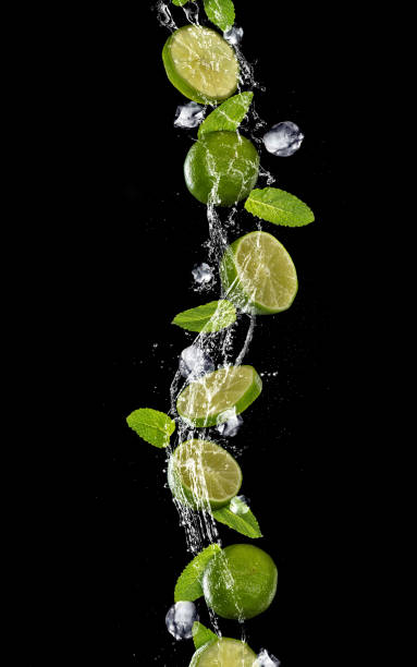 istock Slices of lime falling in water splash on black background 940967360