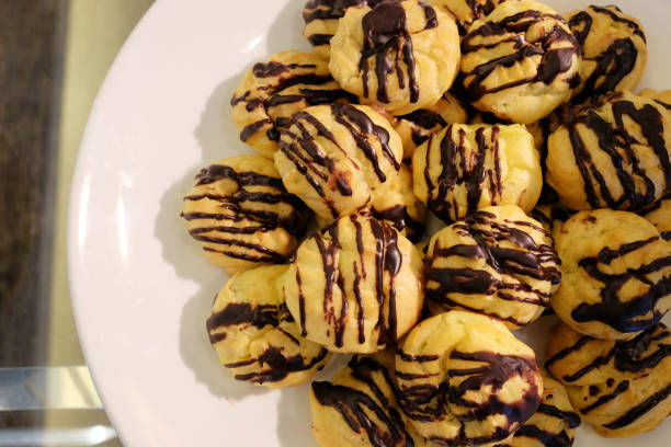 istock Mini mocha eclair with chocolate and whipped cream preparing on baking sheet. Spreading chocolate on top of eclair with spoon. Traditional French dessert. 940968960