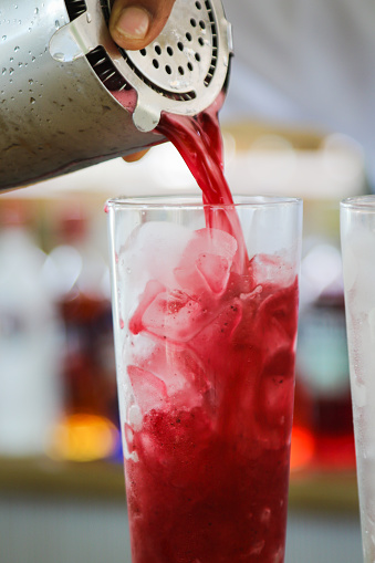 Bartender pouring red drink into ice filled tall glass