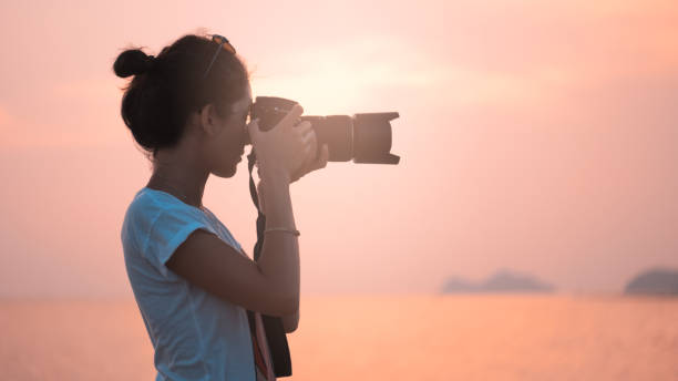 young woman photographer, taking pictures of landscape at sunset stock photo