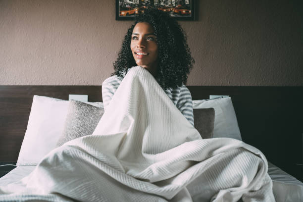 istock Pretty black woman covered with sheet and sit on bed looking away 940981750